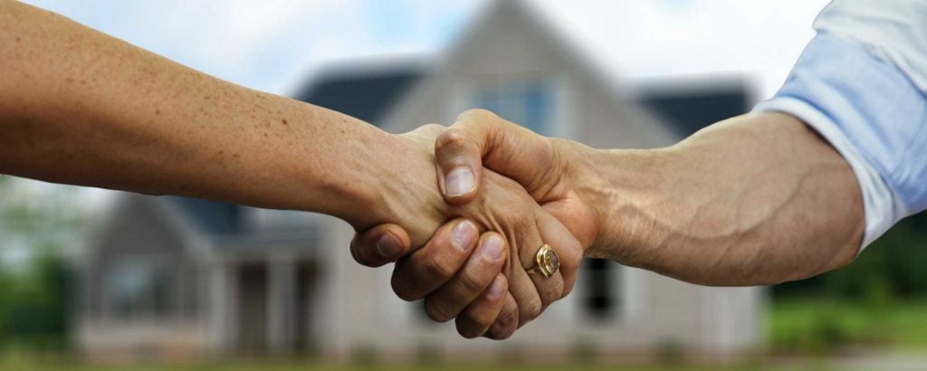 Two men shake hands in front of a home.