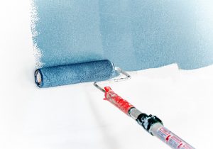 Roller with blue paint on wall