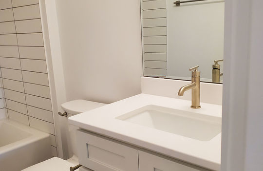 A full sized guest bathroom with white subway tile and white vanity.