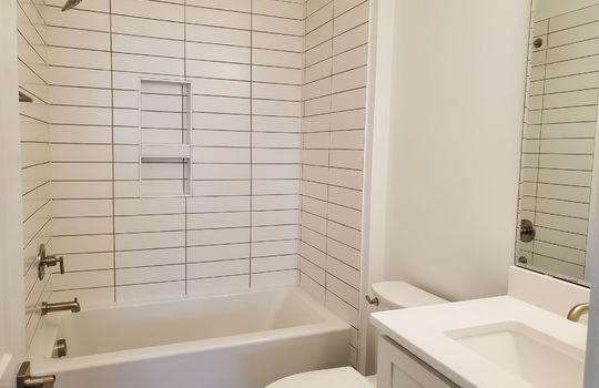 A full sized guest bathroom with white subway tile and white vanity.