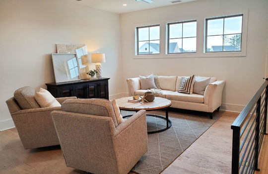 A second-floor loft with 3 square windows, a couch, two armchairs, and a sideboard.