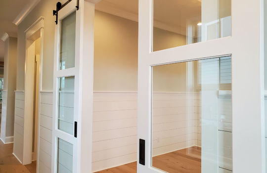 The sliding doors on a home office with half-wall paneling.