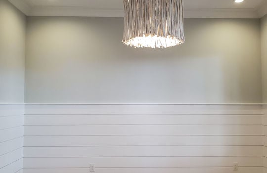 A home office with half-wall horizontal paneling, recessed lighting, and a driftwood penant light.