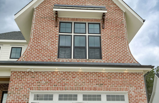 Recessed lights over a white garage door and a unique Tudor style roof line.
