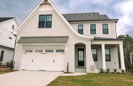 The front of a gray home with a white garage door and a Tudor style roof curving over the front entrance.