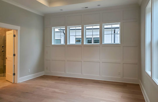 A primary bedroom with a trey ceiling and paneled wall with 4 small windows.