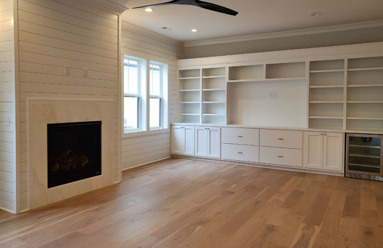 A full built-in wall of shelves and cabinets with a space for a TV and a gas fireplace surround by marble and shiplap.