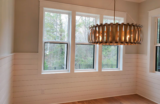 Dining room with a slatted wood pendant light, large windows, and a half-wall of horizontal paneling.