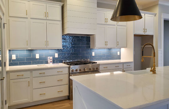 A large kitchen with white double cabinets, a large island, and blue tile.