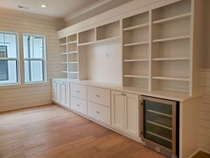 A full built-in wall of shelves and cabinets with a space for a TV and a wine fridge..