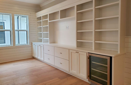 A full built-in wall of shelves and cabinets with a space for a TV and a wine fridge..