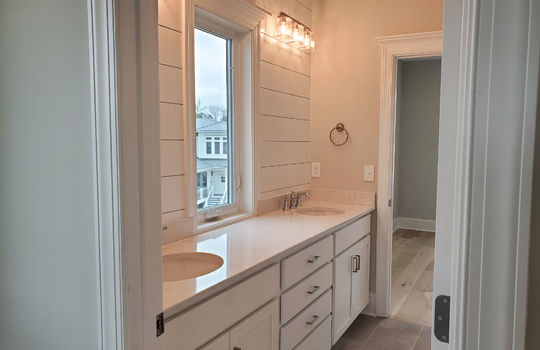 A bathroom with a large double vanity, ship-lap, overhead glass triple sconces, and a window between mirrors.