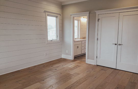 A primary bedroom with double doors too closet, doorway to attached bathroom, and an accent wall with shiplap paneling.