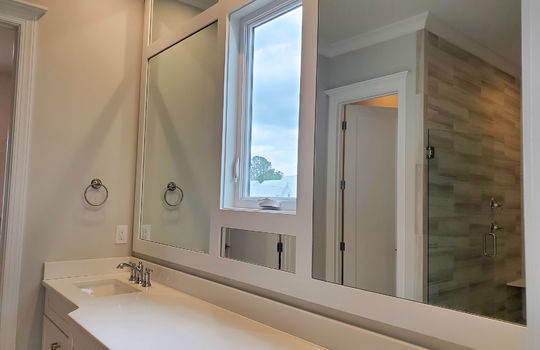 A large double vanity with a wall of mirrors broken up by a single small window.