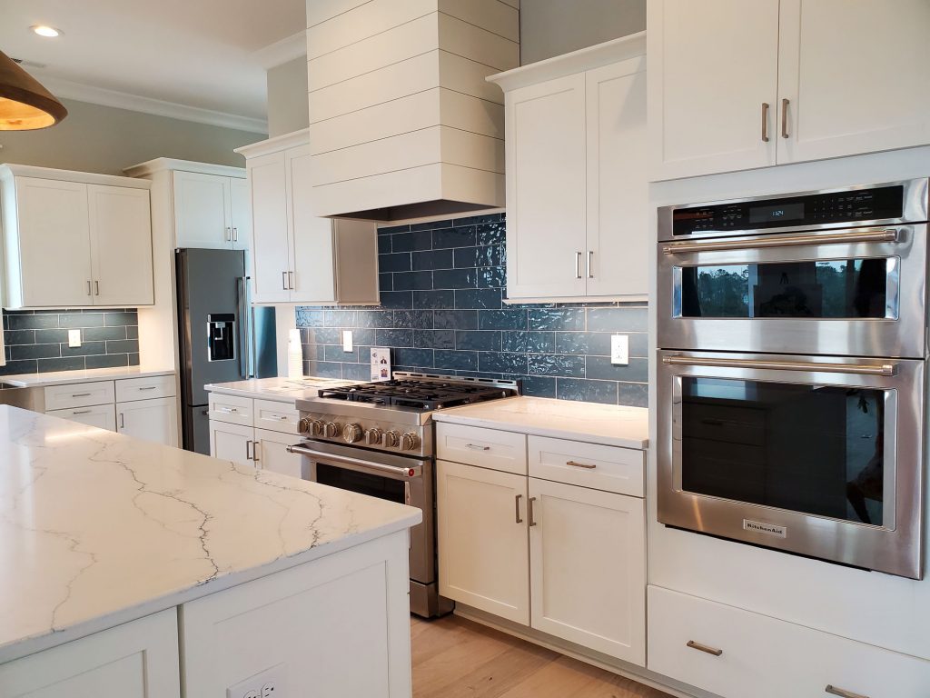 A gourmet kitchen with white cabinets, blue tile, and stainless steel appliances, including a gas stove.