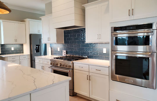 A gourmet kitchen with white cabinets, blue tile, and stainless steel appliances, including a gas stove.