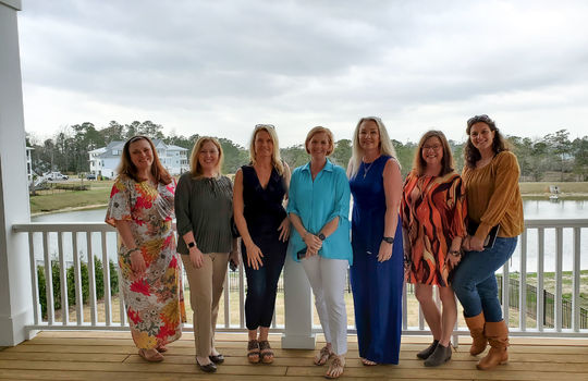 7 members of The Cameron Team standing on a deck overlooking the pond.