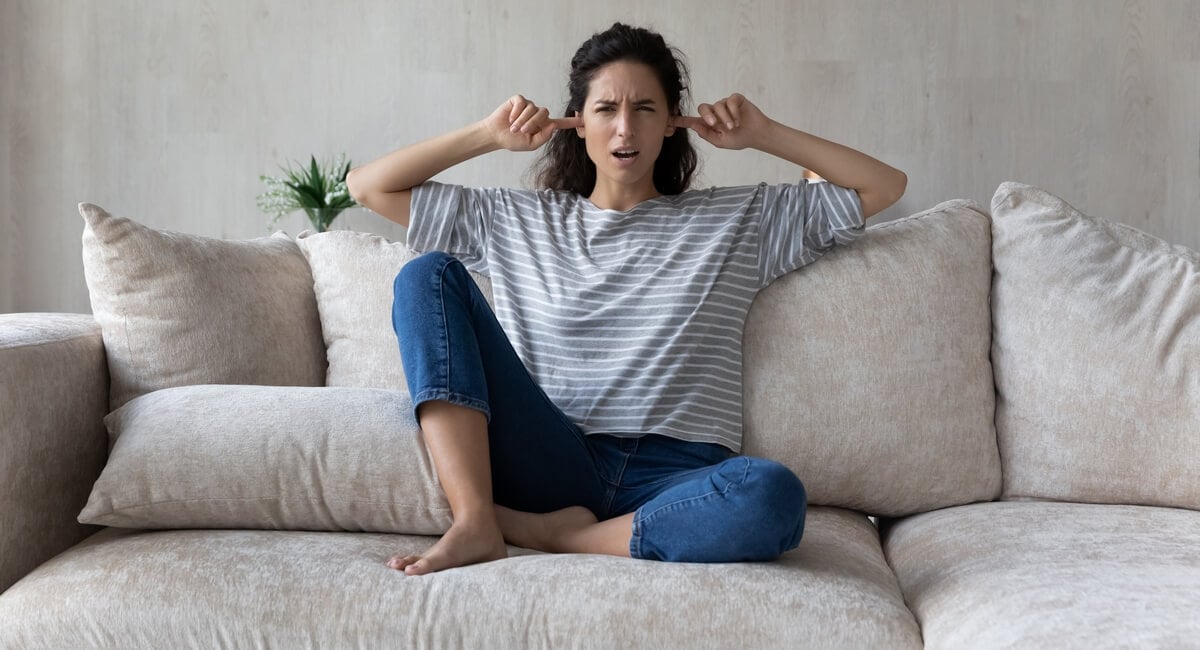A woman plugging her ears while sitting on a couch.