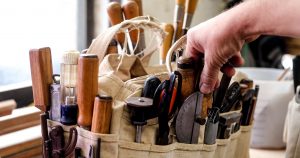 Man selecting a hand tool from a bag on workbench