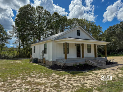 Angled front view showing white farmhouse exterior, black metal roof and covered front porch