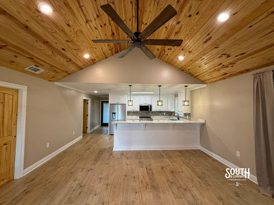 Vaulted pine ceiling with ceiling fan and open view from the living area toward the kitchen