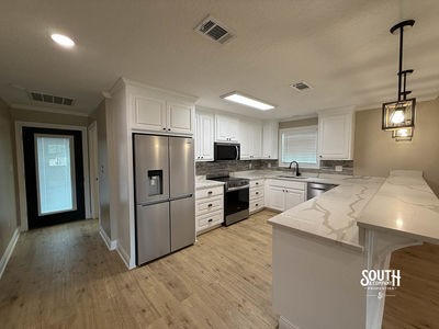 Kitchen with white cabinetry, Corian countertops, stainless appliances and eat-in bar