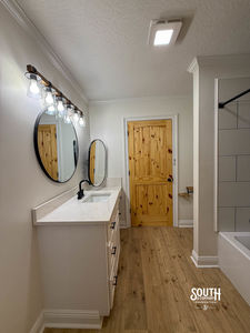 Bathroom vanity with round mirrors, light fixtures and tub-shower area