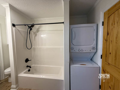 Stacked washer and dryer beside tub-shower in a utility bathroom