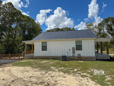 Side view of white farmhouse with black metal roof and wooden rear deck